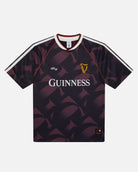 A short-sleeve Guinness football jersey with a dark purple and black geometric pattern, featuring the white 'GUINNESS' sponsor logo on the chest, a gold harp crest, and white shoulder stripes.